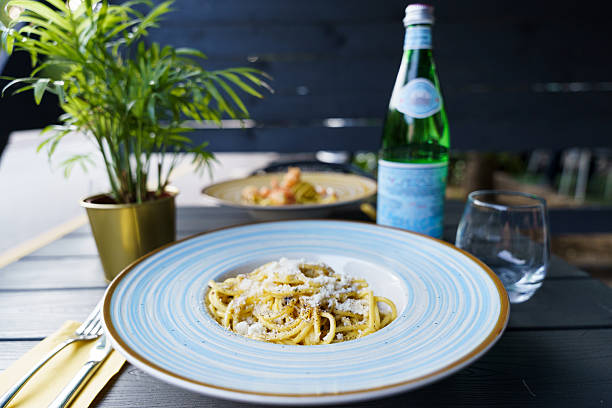 A plate of authentic Italian cacio e pepe pasta, featuring al dente spaghetti coated with Pecorino Romano cheese and freshly ground black pepper. The dish is served in a blue-striped ceramic bowl.