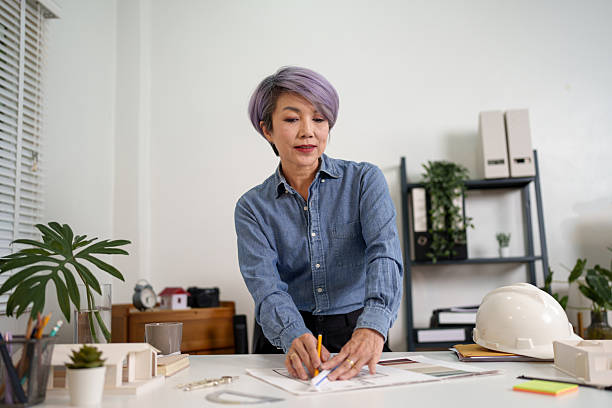 istock Asian Women Architect Design Blueprint Drawing Plan Construction Building Project by Engineer Professional For Architecture Designs and Construction Projects 2216972677