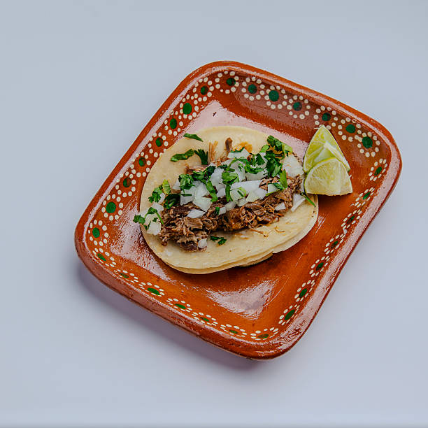 istock Authentic Mexican taco with shredded beef, onion, cilantro, and lime on handmade clay plate, isolated on white background 2216974298