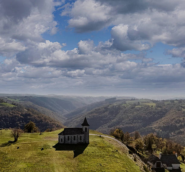 Perched atop a serene hill in the heart of the Cantal region, this solitary stone chapel gazes over a sea of rolling valleys and forested ridges. Under a dramatic sky pierced with light, the scene evokes a timeless sense of solitude, spirituality, and harmony with nature. A perfect capture of France’s rural soul, where silence speaks and beauty breathes.