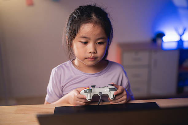 istock Asian Young girl engaged in gaming experience at home, holding game controller while focused on screen, showcasing joyful play and modern technology interaction 2216978453