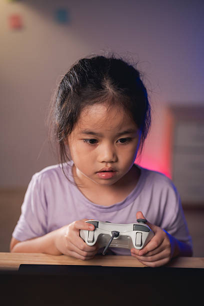 Asian Young girl immersed in gaming, holding video game controller, focused expression, colorful background, engaging in digital entertainment at home