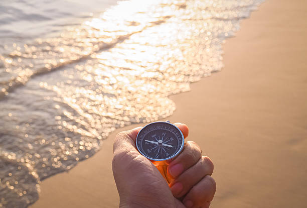 istock Close up hand holding compass with beach background in the sunset time 2216979716