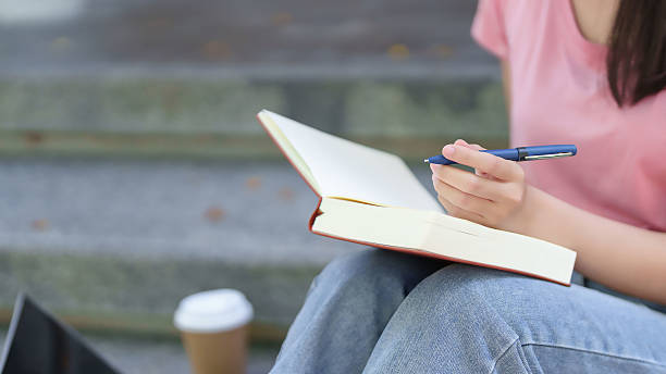 istock Young Asian Woman Studying with Open Book on Steps Education Concept Writing Notes Student Learning Knowledge Academic Studying Lifestyle 2216984543
