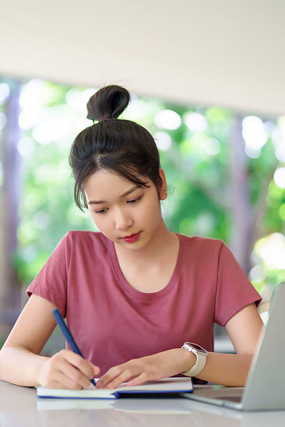 istock Young Asian Woman Studying Writing Notes with Laptop for Education Online Learning Homework Exam Preparation and Research at Home 2216984593