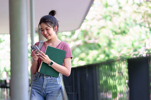 istock Young Asian Woman Student Using Smartphone and Holding Book on University Campus Education for College and Highschool Studying 2216984641