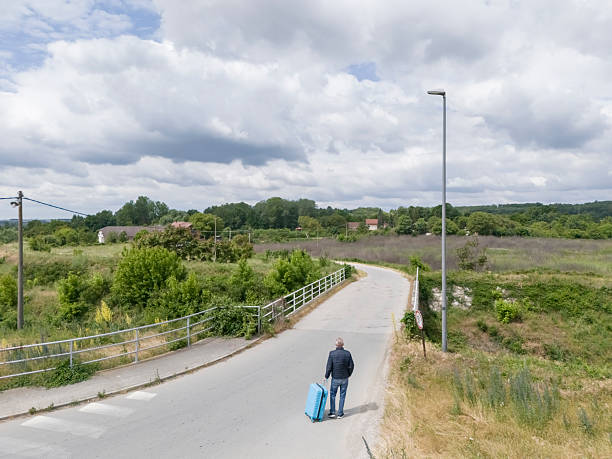 Girl in blue dress with suitcase on country road in summer.