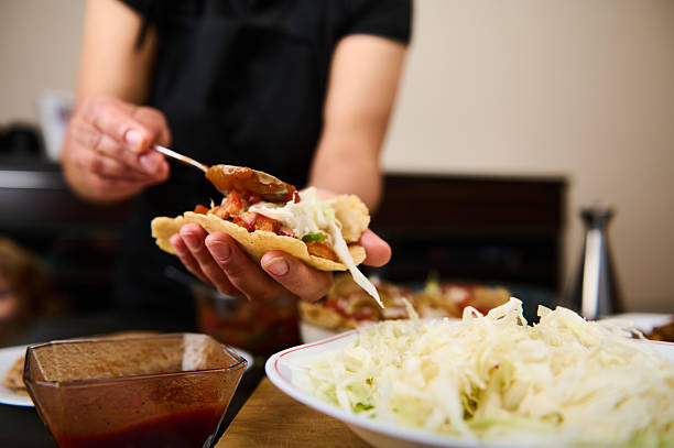 Focused image of hands assembling tacos with fresh toppings such as cabbage and salsa, conveying a warm, inviting mood.
