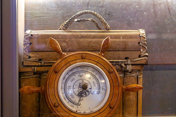 An old-fashioned barometer mounted in a decorative wooden ship wheel frame. A classic maritime weather instrument with nautical design.