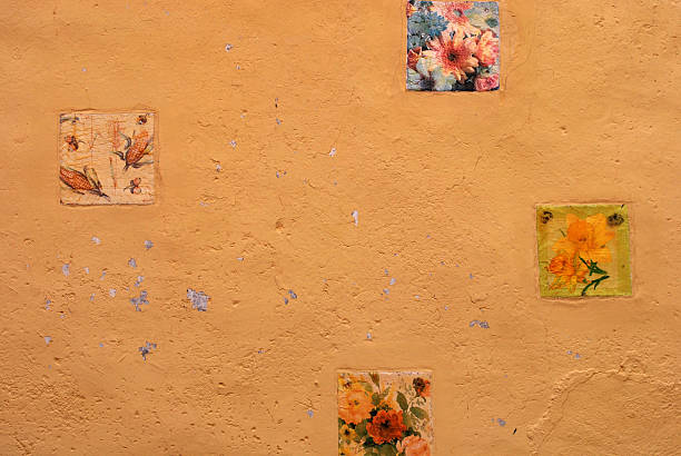 A charming ochre wall in Maratea is decorated with four painted ceramic tiles, each depicting delicate botanical motifs. The vivid colors contrast beautifully with the textured stucco, offering a glimpse of local artisan flair.
