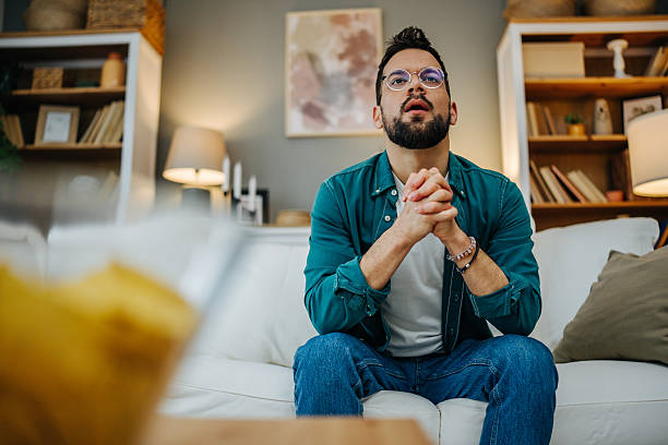 istock Nervous man watching tv at home on sofa holding hands together 2216997175