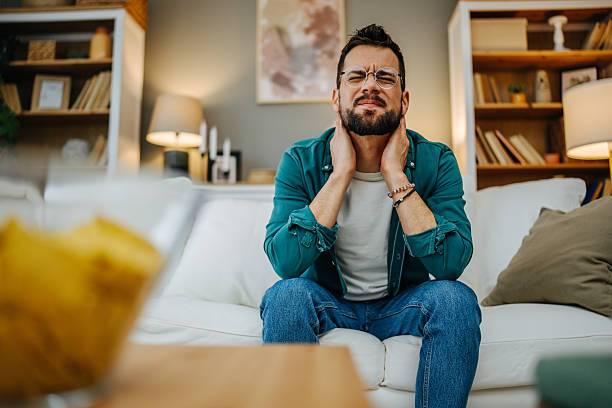 istock Man suffering from neck pain while relaxing on sofa at home 2216997790