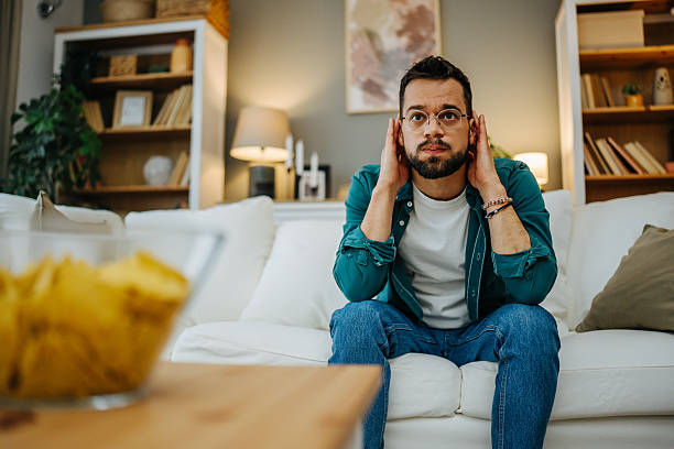 istock Stressed young man covering ears while watching tv at home 2216997793