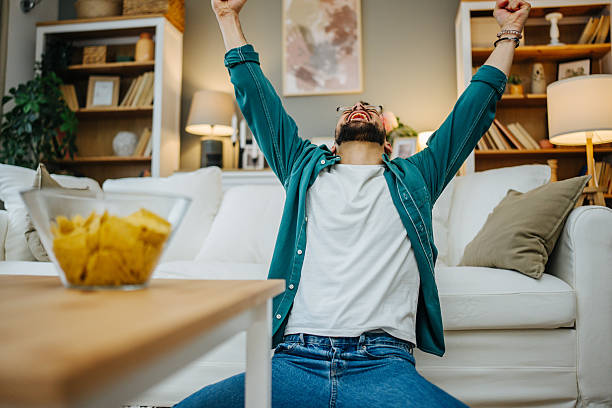 istock Excited young man celebrating success while watching tv at home 2216997877