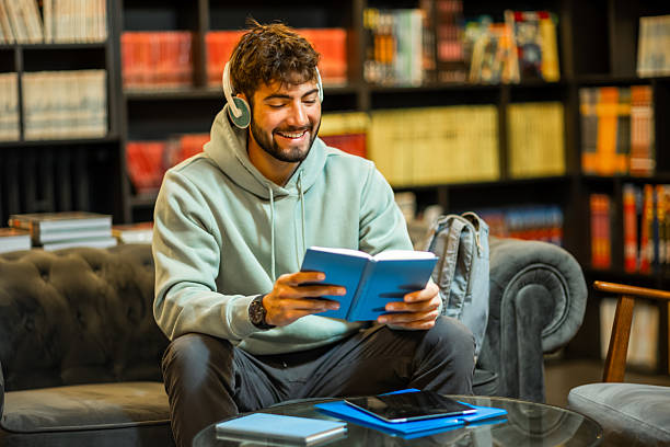 istock Male Student Studying with Book and Headphones in Library 2217000014