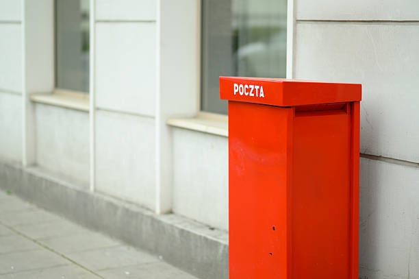 A vibrant red postal box labeled 'poczta' is positioned next to a contemporary building on a clear day, drawing attention.
