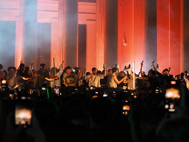 Athens, Greece - May 3, 2025: Silhouettes of people at a concert with raised arms, bathed in orange light against columned backdrop during Athens City Festival 2025