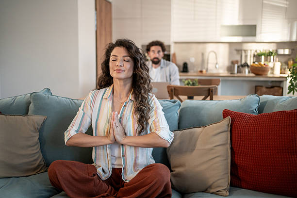 istock Serene woman meditating on sofa while man works on laptop in background 2217009324
