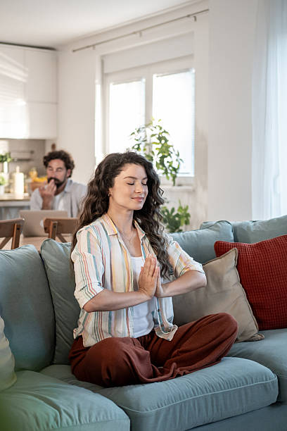 istock Serene woman meditating on sofa while man works in background 2217009389