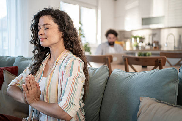 istock Serene woman meditating on sofa while man works on laptop in background 2217009402