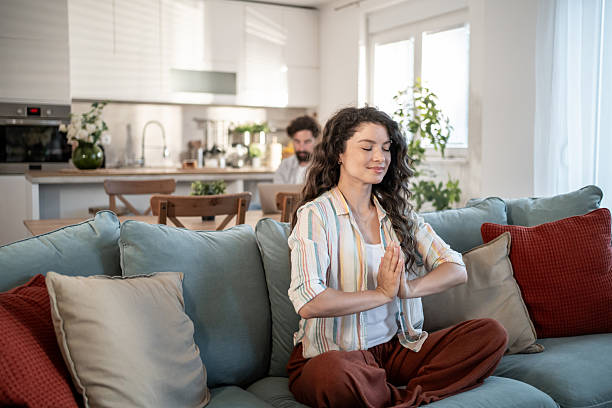 istock Serene woman meditating on sofa while man works in background 2217009403