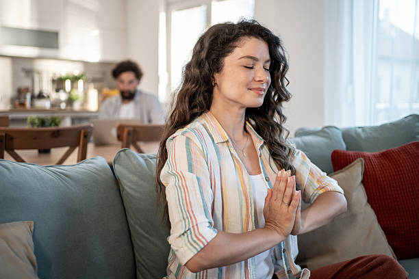 istock Serene woman meditating on sofa while man works on laptop in background 2217009408