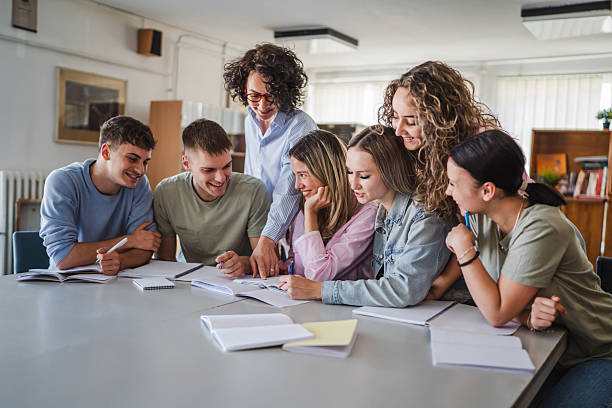 Group of high school students work on project with teacher in library