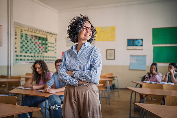 A mature female teacher stand confidently in her elementary classroom