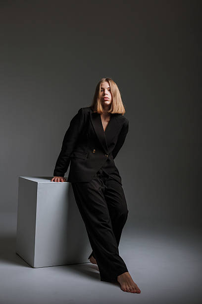 istock Stylish woman in a black suit poses on a white cube in a minimalist studio setting during a photoshoot 2217013490