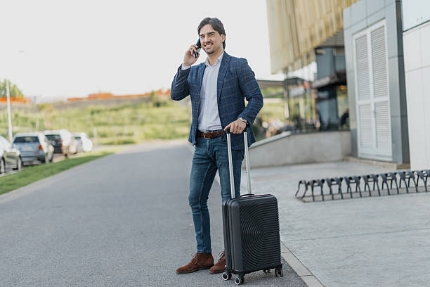 istock Businessman on phone with suitcase outside building 2217021285