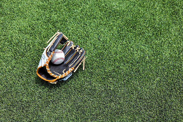 Baseball glove and ball on grass in brightly lit outdoor stadium. Focus on foreground and shallow depth of field on background with copy space. Fictitious background stadium created entirely in Photoshop.