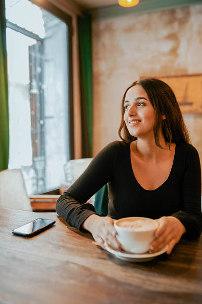 istock Cheerful young woman having coffee looking sideways in cafe 2217033520