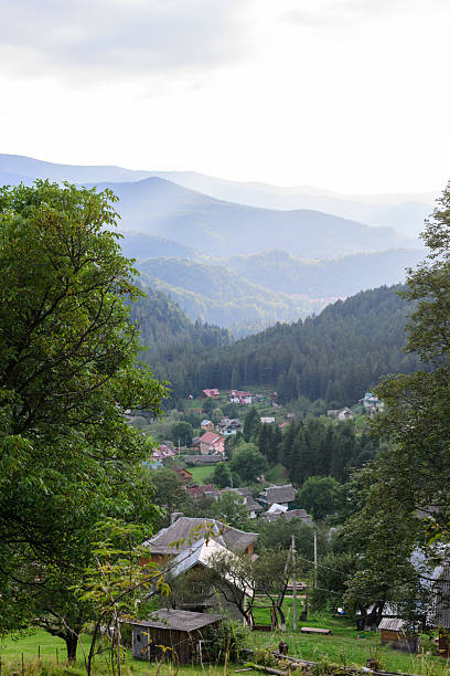 istock Tranquil mountain village vista. Lush trees frame a valley dotted with homes, under soft, layered mountains. Serene landscape, perfect for travel, nature, or lifestyle. 2217039972