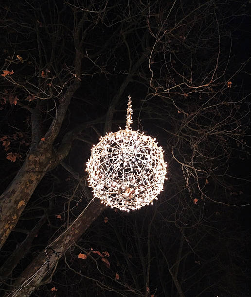 Magical light sphere hanging in a tree against a dark night sky. Evokes a festive, celebratory mood. Perfect for holiday, event, or atmospheric themes.