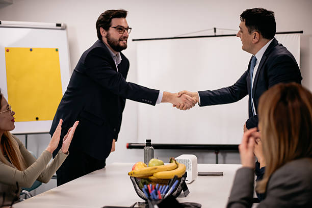 istock Professional colleagues shaking hands during a business meeting in a modern office setting with supportive teammates observing the interaction. 2217040490