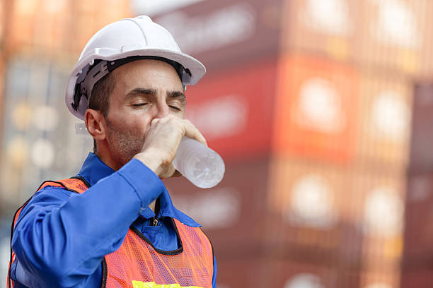 istock Worker man in hard hat drinking water at containers cargo blurred background 2217042776