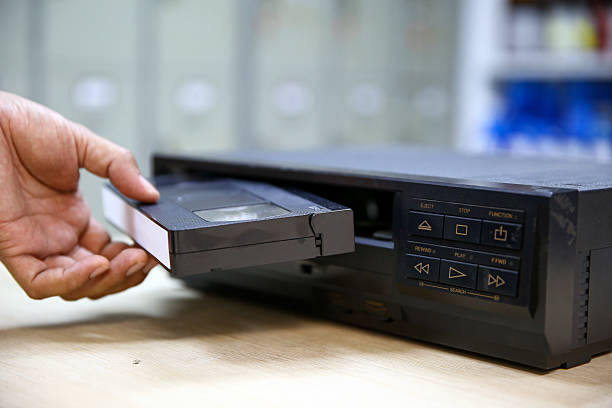 istock Close-up hand put or insert video cassette tape VHS old retro style stack on video record player concept of vintage electric and electronic appliances multimedia player device old fashioned. 2217051814
