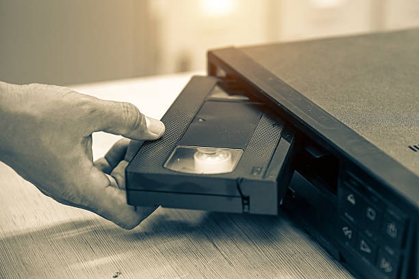 istock Close-up hand put or insert video cassette tape VHS old retro style on video record playback concept of vintage electric and electronic appliances multimedia player device old fashioned. 2217052934