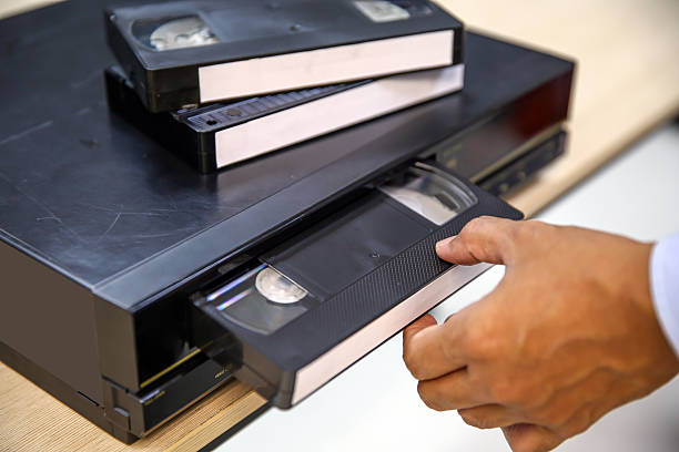 istock Close-up hand put or insert video cassette tape VHS old retro style on video record playback concept of vintage electric and electronic appliances multimedia player device old fashioned. 2217054115