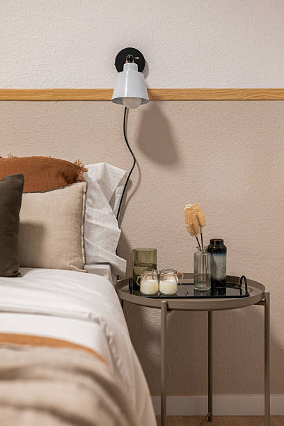 istock Cozy bedroom corner with beige bedding pillows and a side table with candles vases and decorative items 2217073470