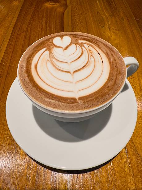 A cup of hot chocolate with beautiful latte art on a wooden table, showcasing intricate design in a cozy cafe setting.