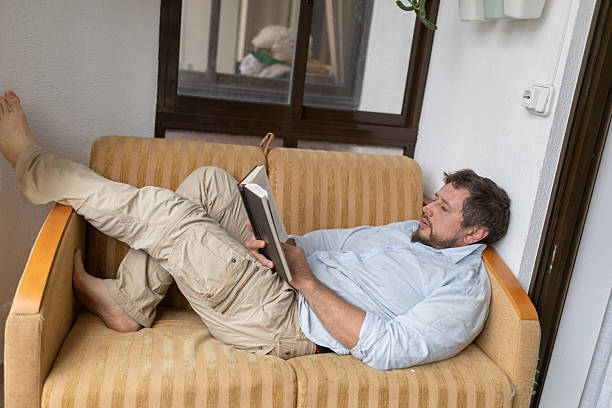 istock Man relaxing on sofa reading a book on balcony 2217076726