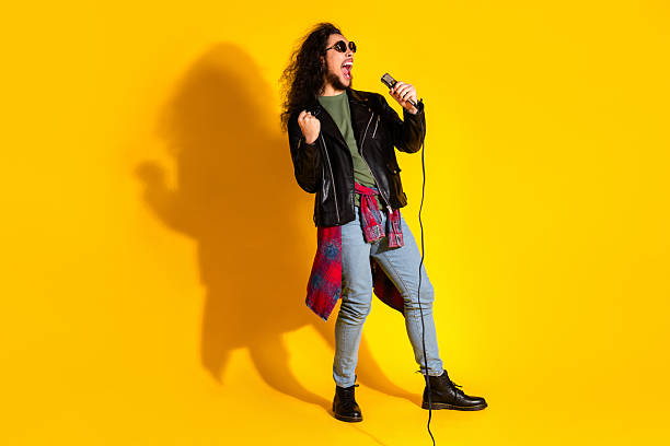 istock Stylish young man with a microphone passionately singing in a pose against a vibrant yellow background 2217083074