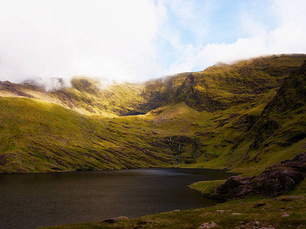 istock Lough callee landscape displaying calm waters surrounded by vibrant green mountains under a partly cloudy sky in County Kerry, Ireland. 2217086429