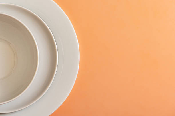 A neatly arranged stack of white ceramic plates in a professional restaurant kitchen. The monochrome aesthetic emphasizes cleanliness, organization, and efficiency in food service. The repetitive pattern and soft lighting create a minimalist yet elegant atmosphere, making this image ideal for hospitality branding, restaurant supply promotions, and kitchen management visuals.