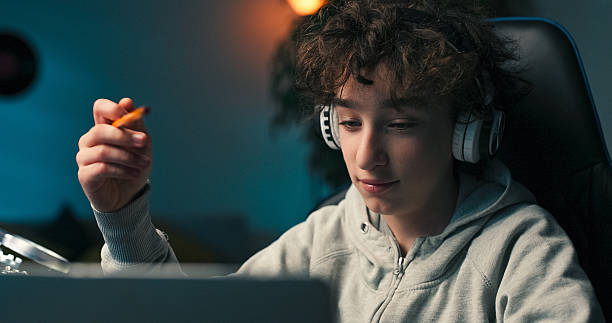 istock A student sits in a room with wireless headphones, taking notes and sketching. His curly hair frames his face as he pauses to reflect on what to do next. 2217088099