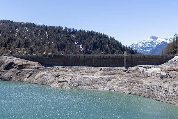 Hydropower generated from arch dam and reservoir lake in snow covered Swiss Alps mountains to produce renewable energy, sustainable hydroelectricity, aerial drone view, cold autumn weather