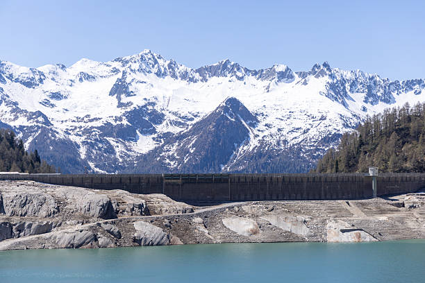 Large dam with turquoise reservoir set against snow-capped mountains. Sturdy construction in a natural landscape. Perfect for environmental and engineering themes.