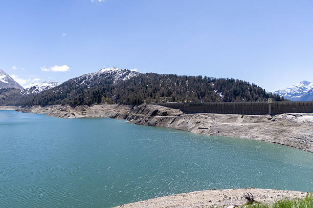 Ebro Reservoir showing clear blue lake water, green rolling hills, a small village, and forested mountains under a partly cloudy sky