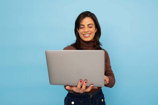 istock Female professional working on laptop, radiating happiness with bright blue backdrop, embodying digital workplace enthusiasm 2217095496